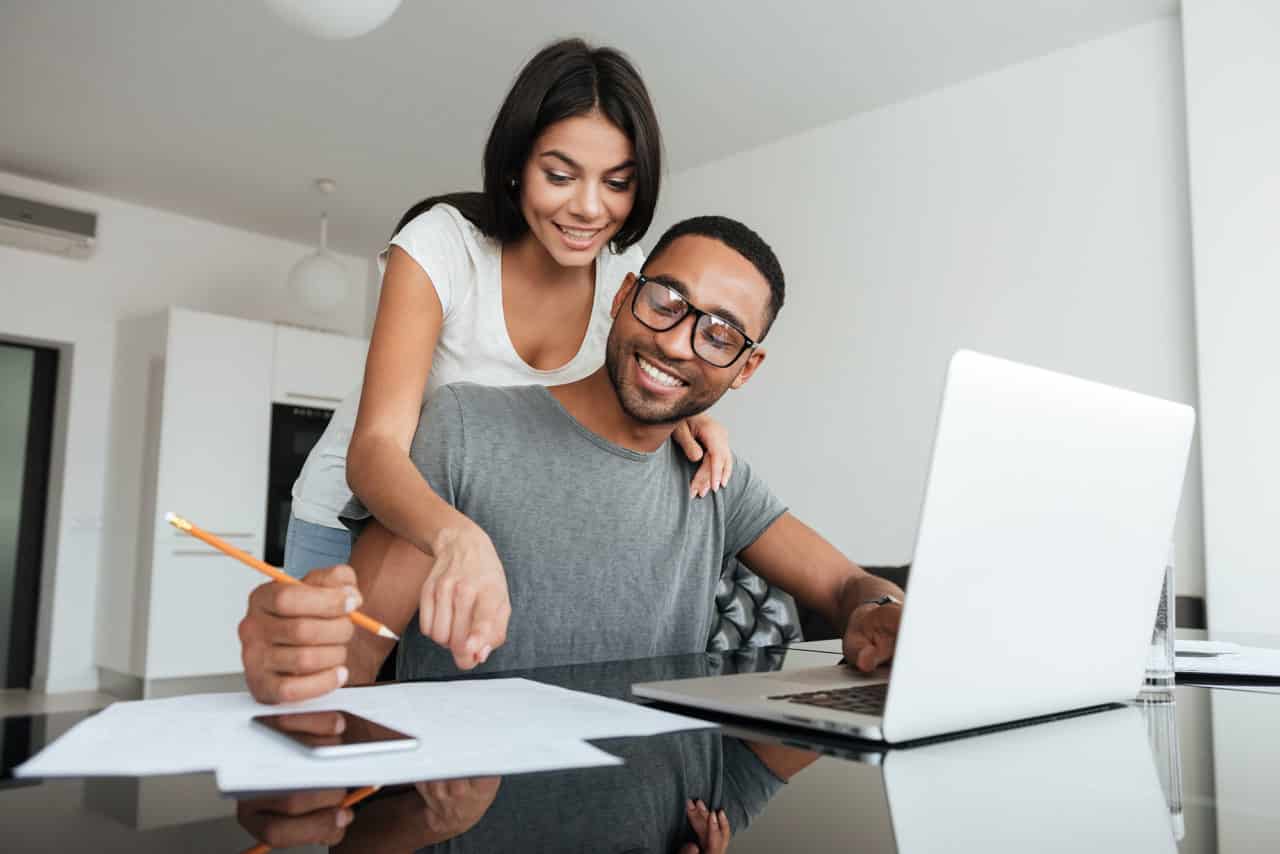 Loving young couple using laptop and analyzing their finances. Writing notes.